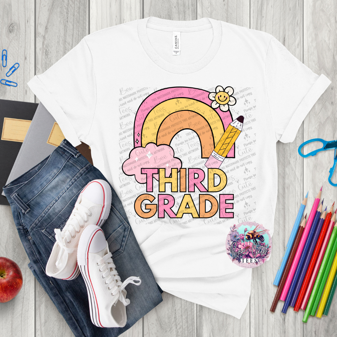White t-shirt with 'Third Grade' design on a wooden surface with jeans, sneakers, and school supplies.