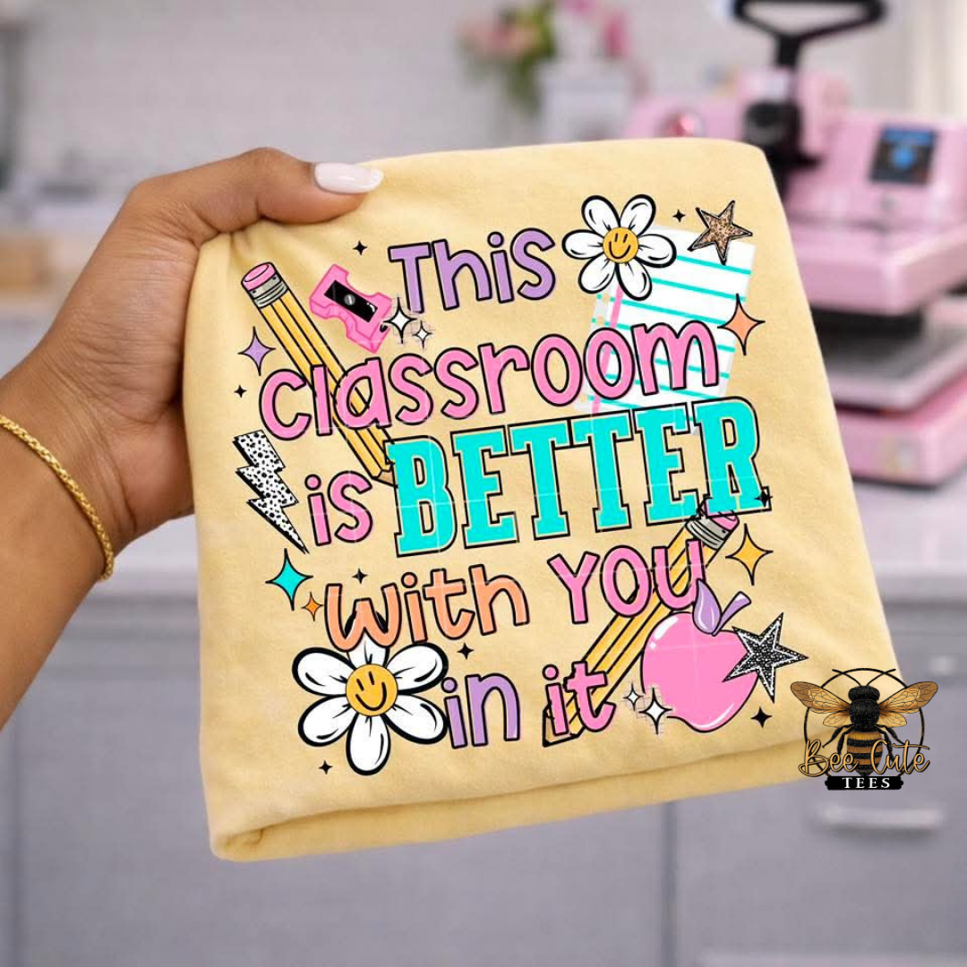 Hand holding a yellow t-shirt with colorful text and graphics, featuring a classroom-themed design.