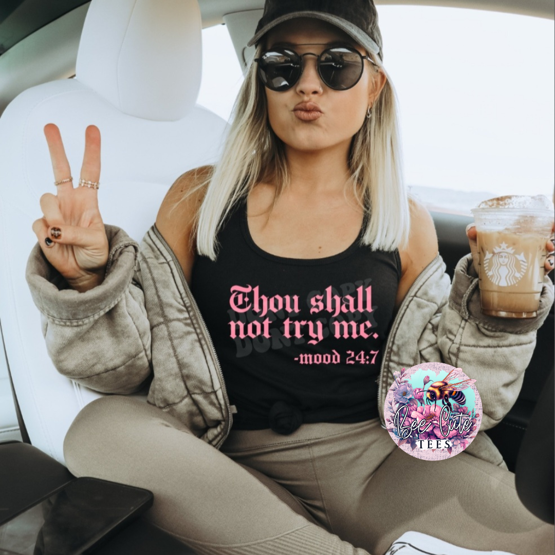 Woman sitting in a car, wearing a black tank top with text, holding a coffee, and making a peace sign.