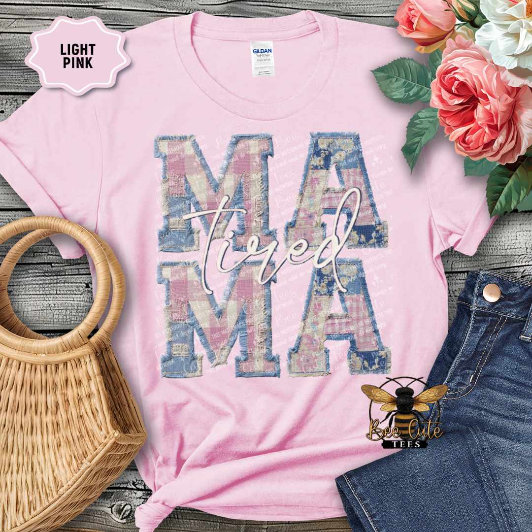 Light pink t-shirt with 'MAMA' design, surrounded by flowers and denim jeans on a wooden surface.
