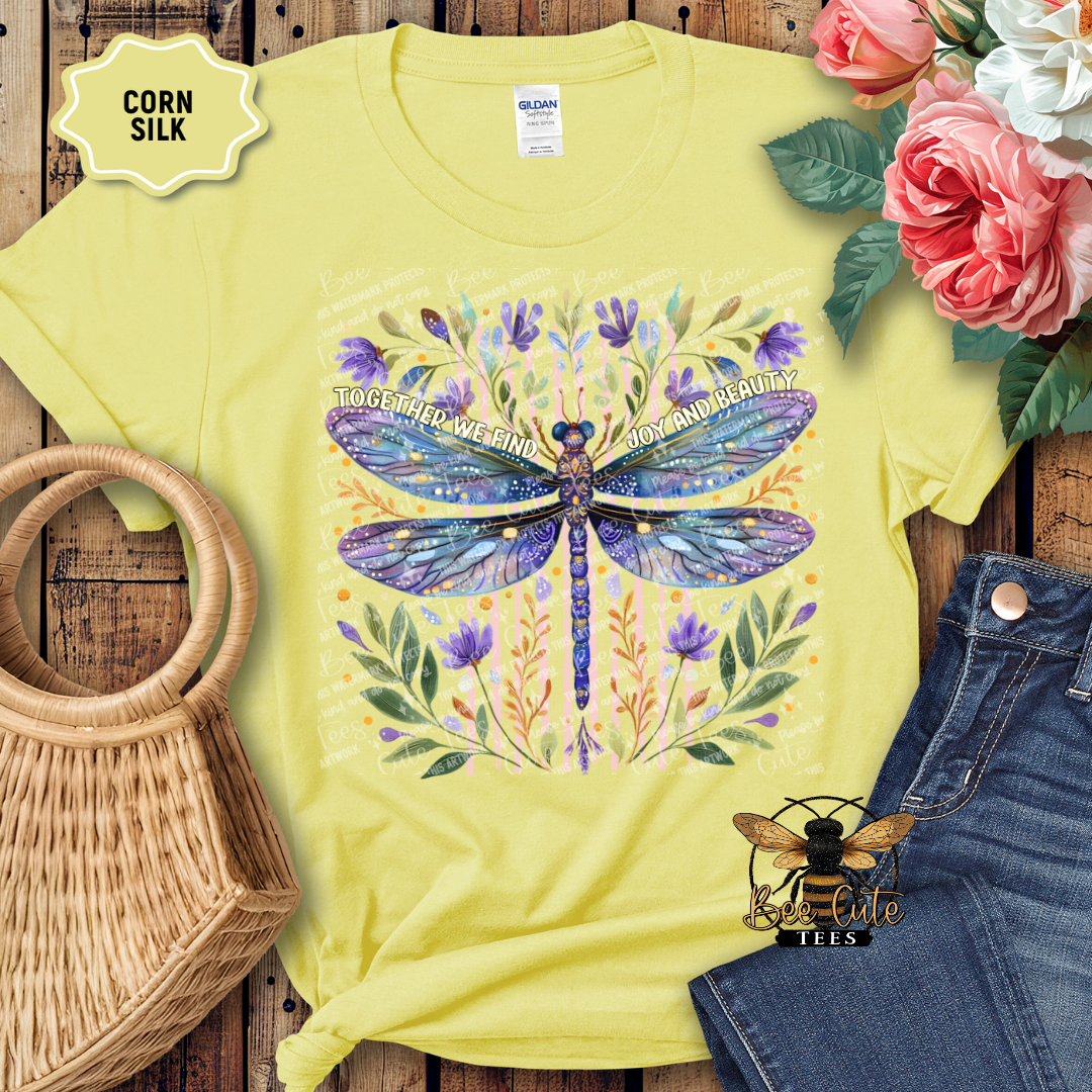 Yellow t-shirt with a dragonfly design on a wooden surface with flowers and denim jeans.