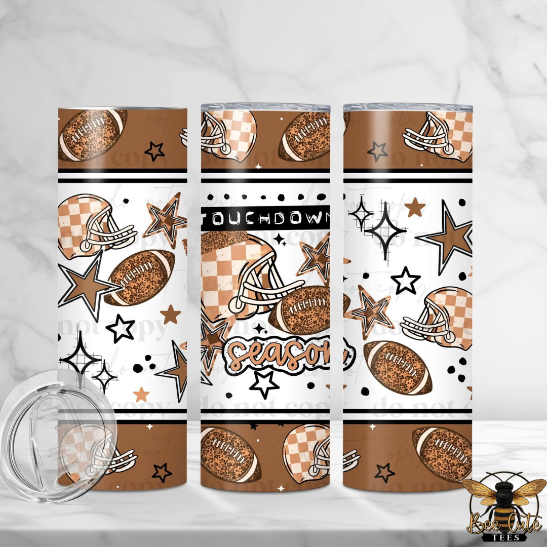 Three tall skinny tumblers with a brown, white, and black football theme, shown on a white marble background with a clear lid in the foreground.