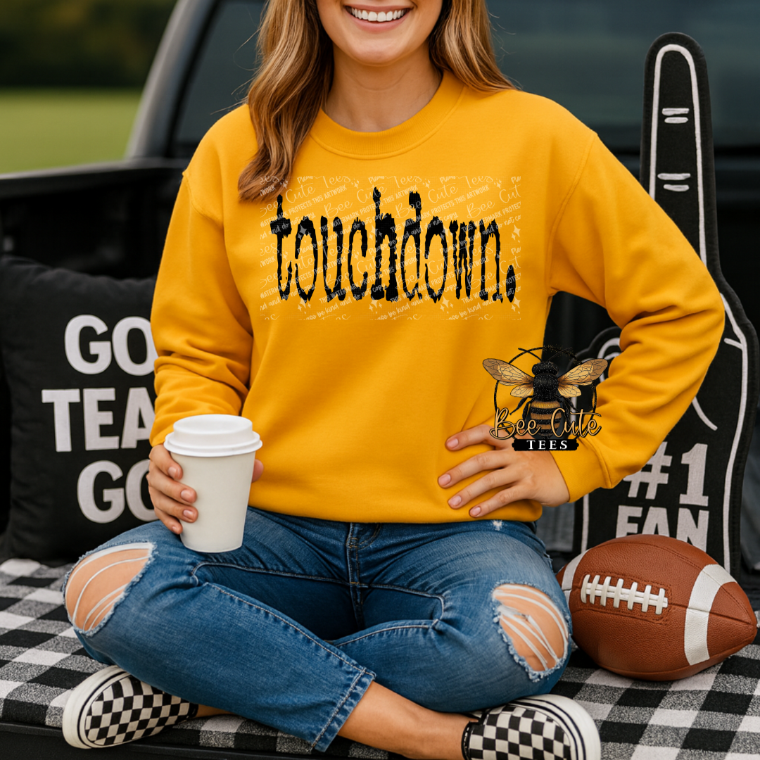 Person wearing a yellow sweatshirt with 'touchdown' text, holding a coffee cup, sitting on a checkered blanket with sports-themed items.