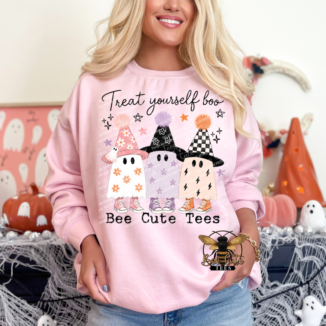 Woman modeling a light pink crewneck sweatshirt featuring three playful pastel Halloween ghosts wearing patterned witch hats and colorful sneakers. The design reads “Treat Yourself Boo” in black cursive lettering above the ghosts and “Bee Cute Tees” underneath. Styled with blue jeans against a festive pink Halloween background.