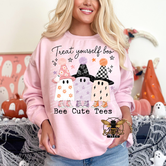Woman modeling a light pink crewneck sweatshirt featuring three playful pastel Halloween ghosts wearing patterned witch hats and colorful sneakers. The design reads “Treat Yourself Boo” in black cursive lettering above the ghosts and “Bee Cute Tees” underneath. Styled with blue jeans against a festive pink Halloween background.