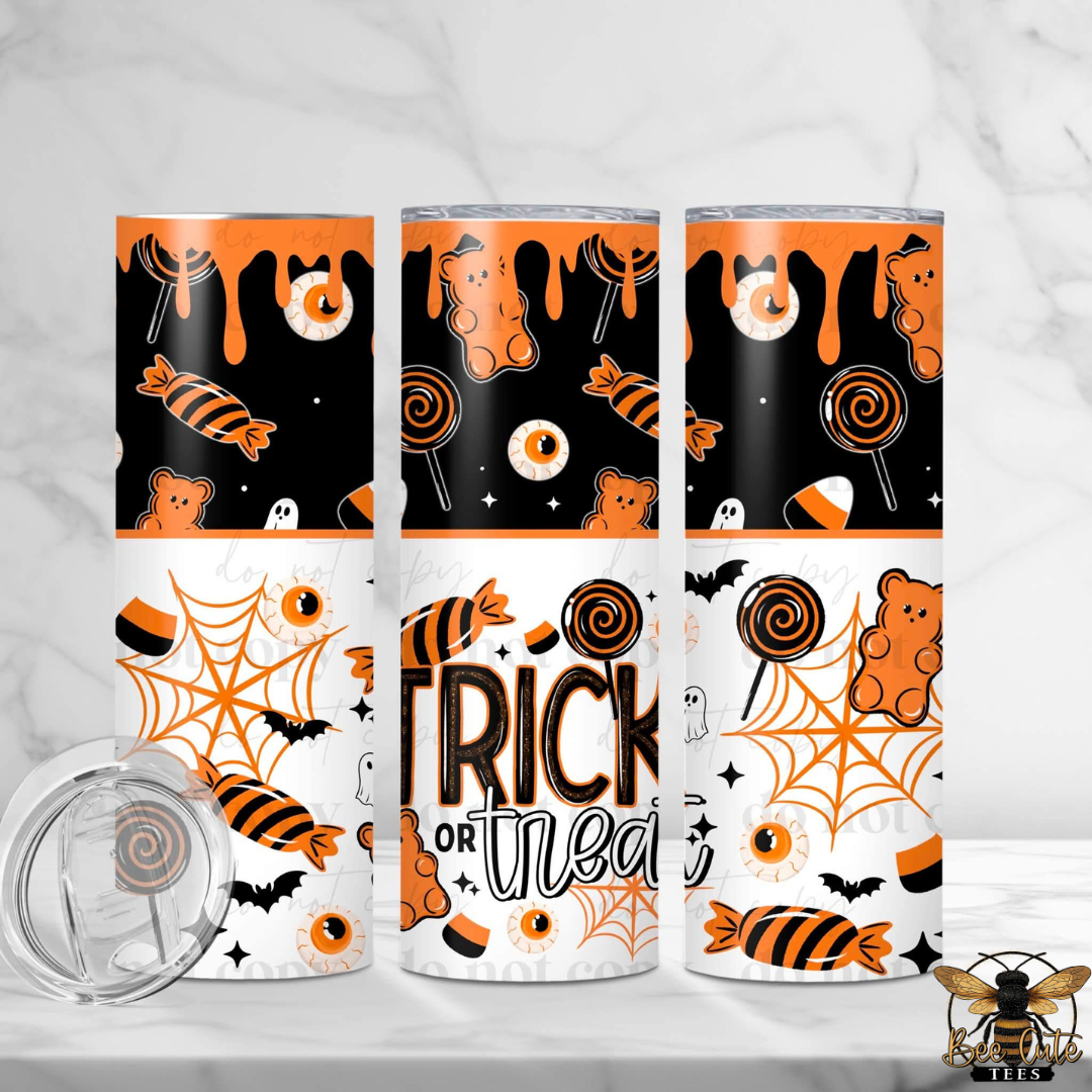 Three tall insulated tumblers with Halloween-themed wraparound prints are shown on a light marble surface. The designs feature orange and black candy, spiderwebs, ghosts, bats, and the words 'Trick or treat.
