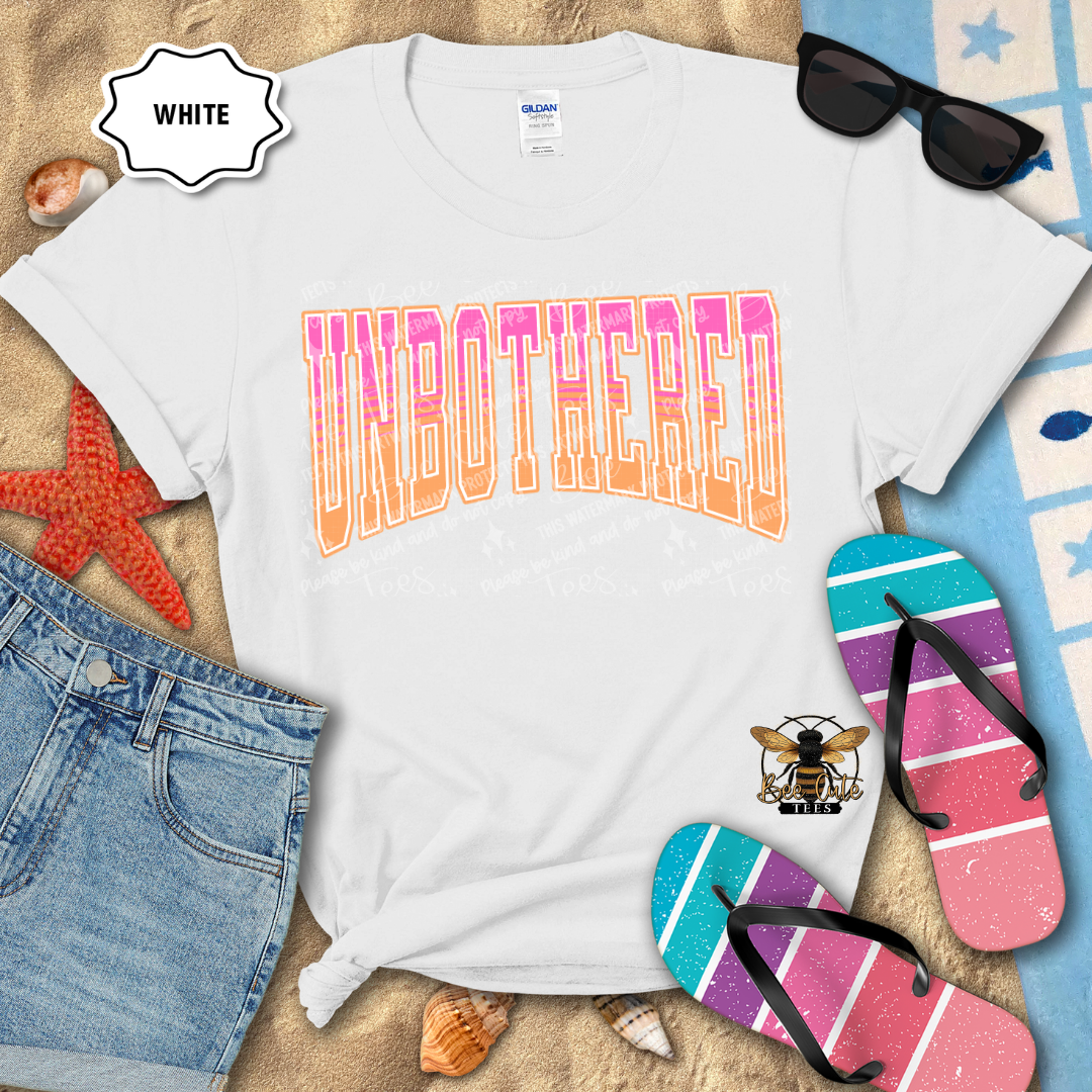White t-shirt with 'UNBOtherED' text, sunglasses, denim shorts, and flip-flops on a sandy background.