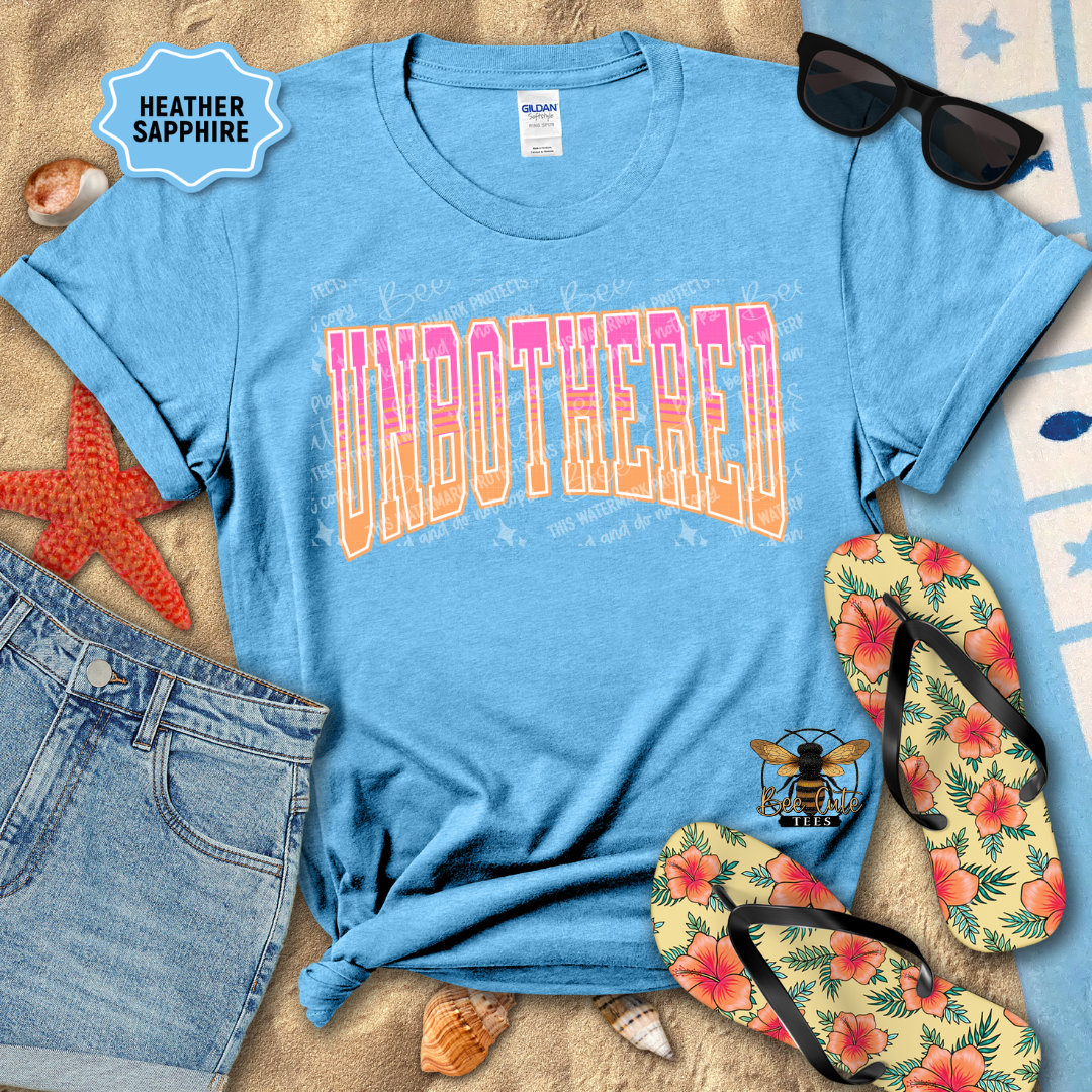 Blue t-shirt with 'UNBOtherED' text, sunglasses, flip-flops, and denim shorts on a sandy background.