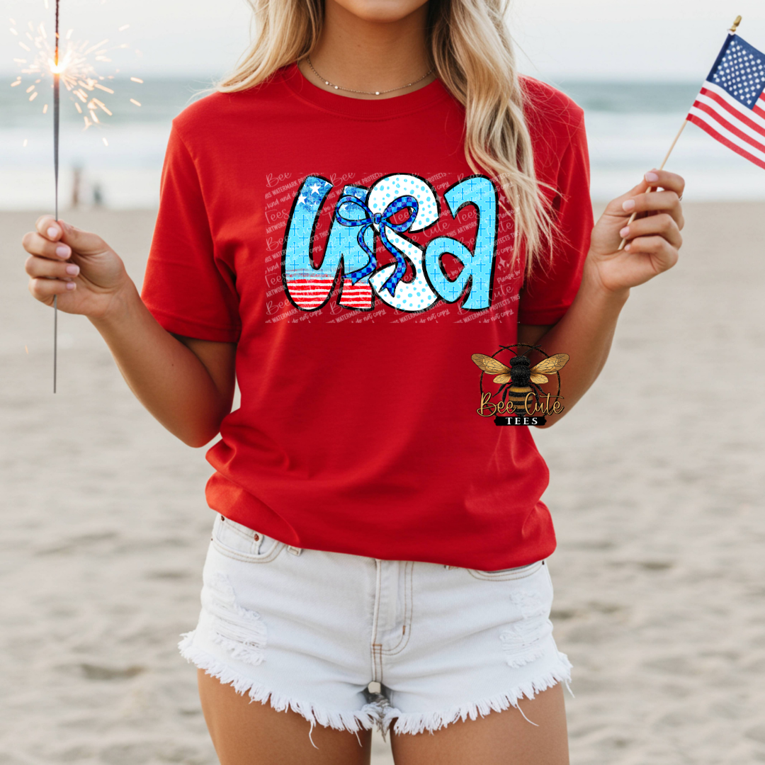Person wearing a red 'USA' t-shirt on a beach with sparklers and an American flag.