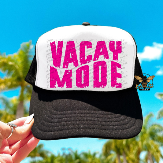 Black and white cap with pink 'Vacay Mode' text held against a blue sky and palm tree background.