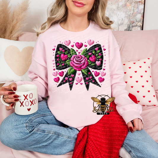 Person wearing a pink sweatshirt with a colorful bow design, sitting on a couch with heart-shaped pillows.