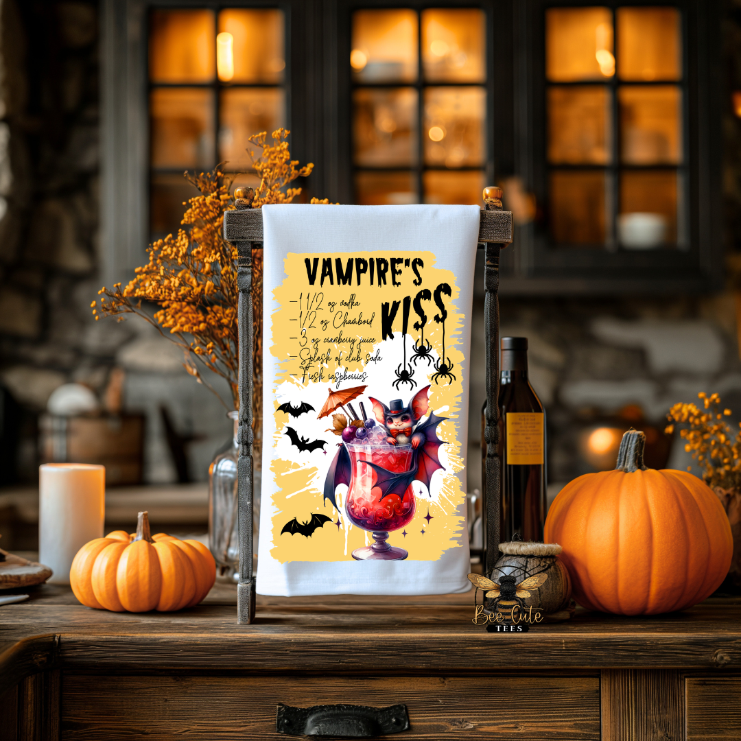 A white kitchen towel with a Halloween-themed vampire graphic and quote, hanging on a wooden stand on a rustic table with pumpkins, candles, and autumn decor in the background.