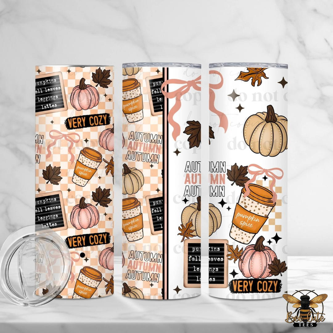 Three views of a stainless steel skinny tumbler with a fall autumn theme, including pumpkins, coffee cups, leaves, and text like 'VERY COZY' and 'AUTUMN AUTUMN'. A clear lid is shown in the bottom left on a white marble background.
