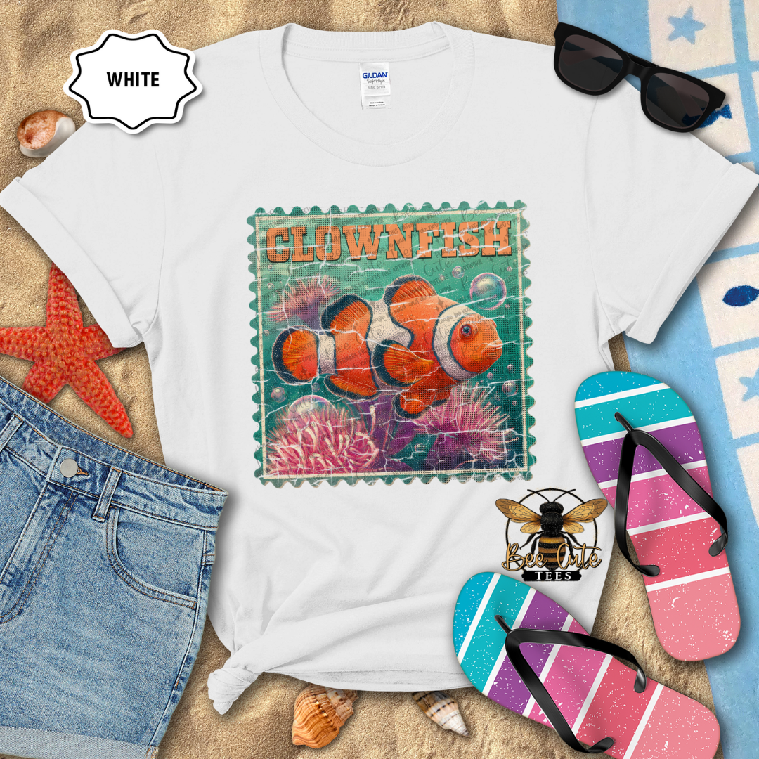 White t-shirt with clownfish graphic on a beach-themed background