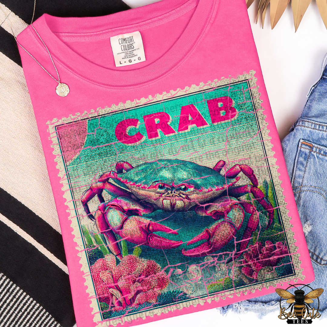 Pink t-shirt with a colorful crab design and 'CRAB' text on a striped fabric background.