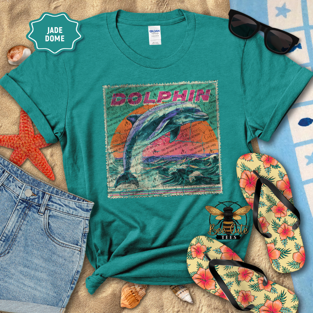 Teal t-shirt with dolphin design, sunglasses, flip-flops, and denim shorts on a beach-themed background.
