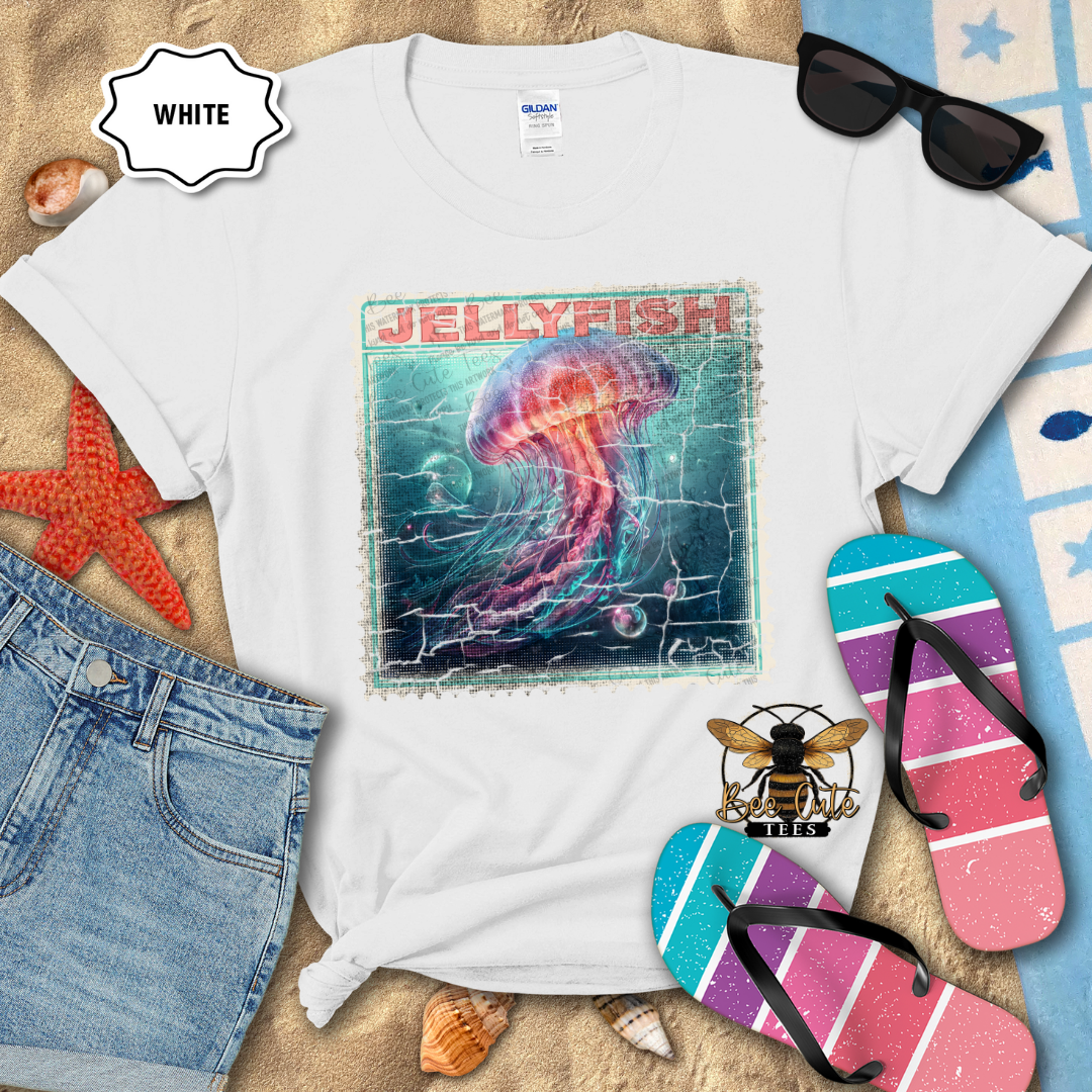 White t-shirt with jellyfish design on a sandy surface with beach accessories.
