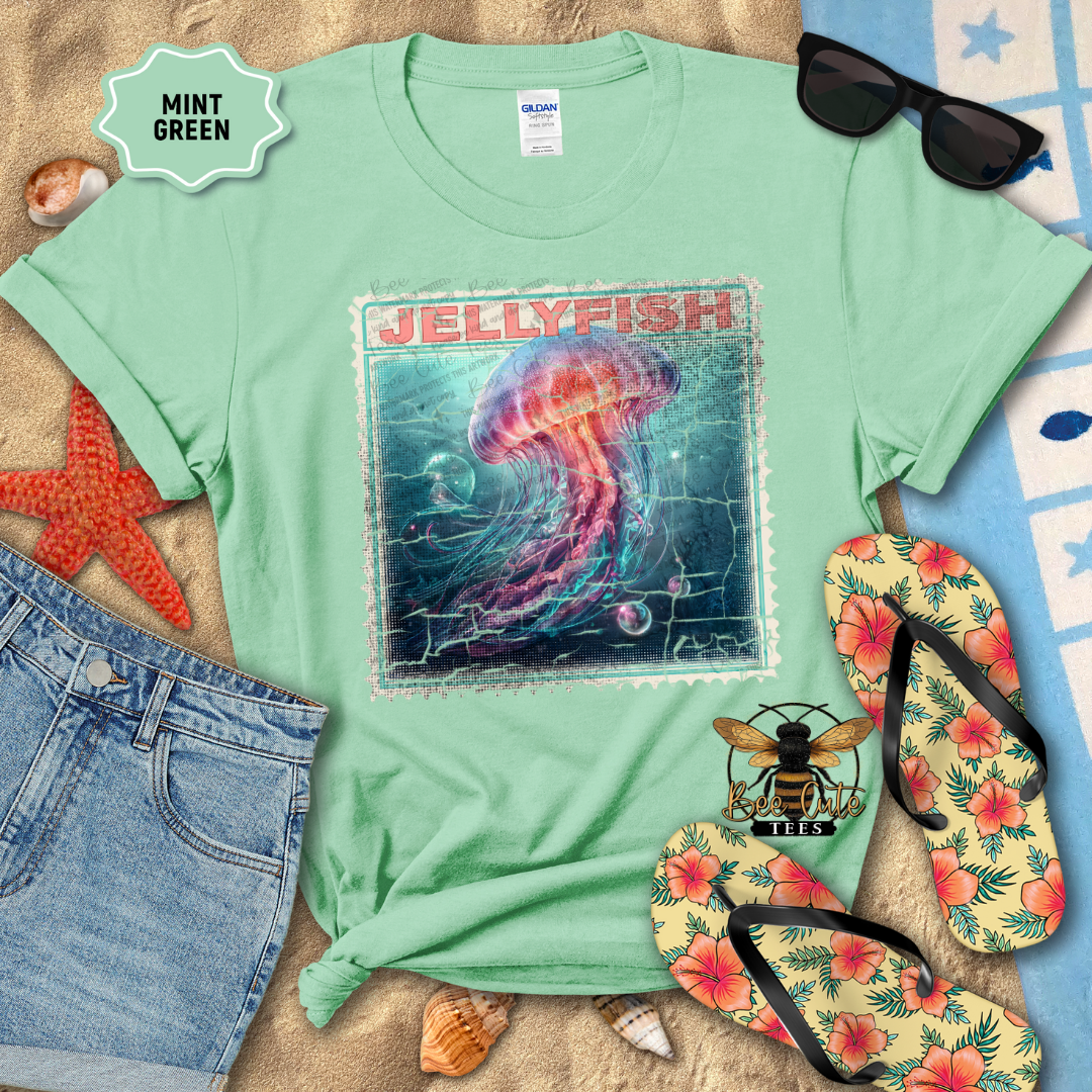 Mint green t-shirt with jellyfish design, sunglasses, and flip-flops on a beach setting.