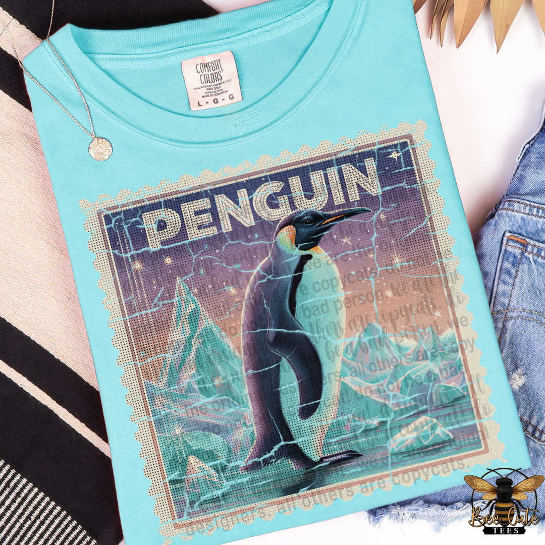 Light blue t-shirt with a penguin graphic and 'PENGUIN' text on a textured background.