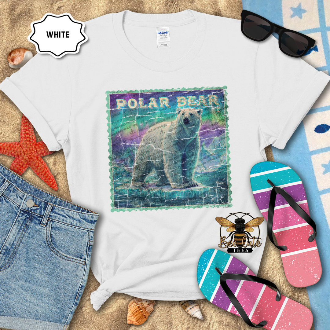 White t-shirt with polar bear graphic on a sandy surface with beach accessories.