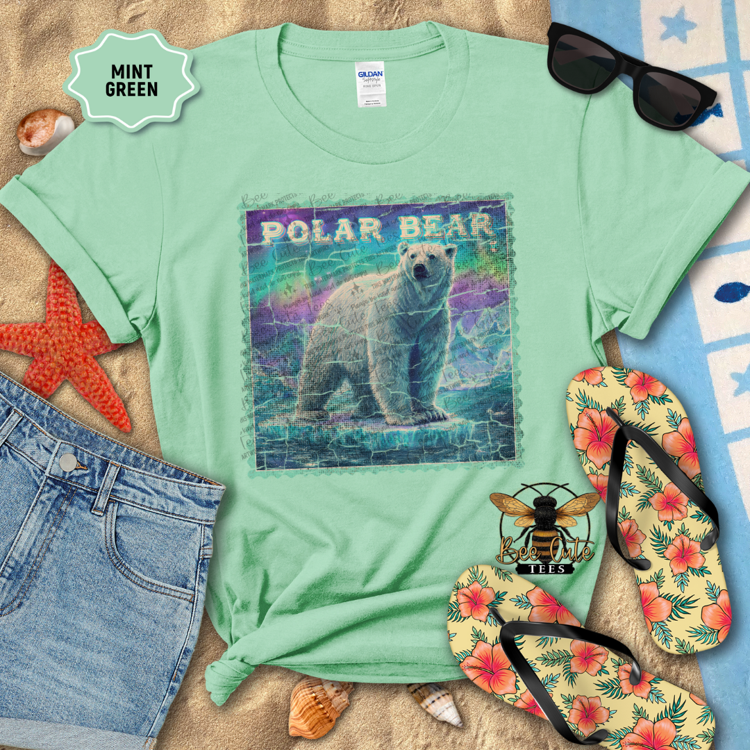 Mint green t-shirt with polar bear graphic on a sandy surface with beach accessories.