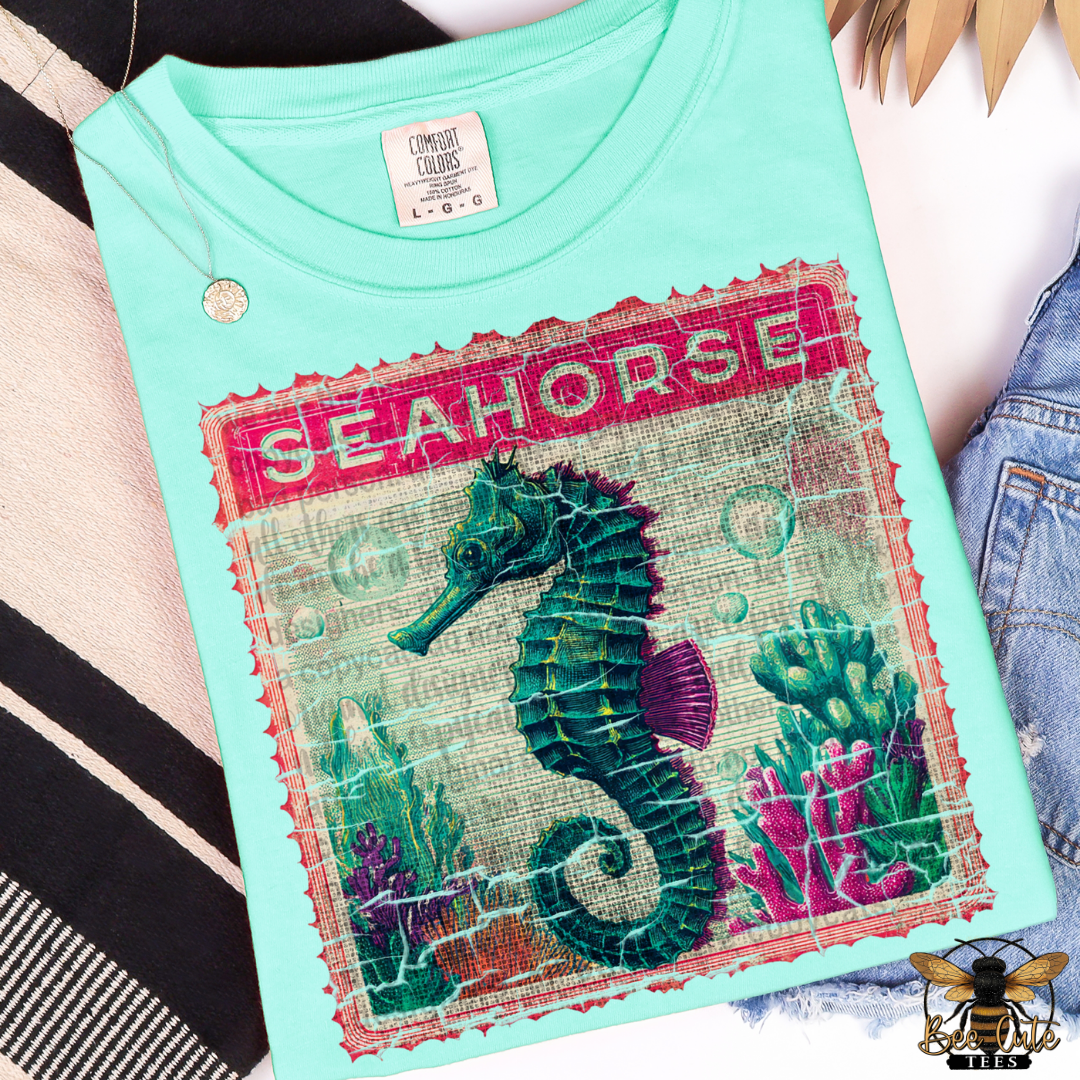 Light blue t-shirt with a seahorse design and 'Seahorse' text on a striped fabric background.