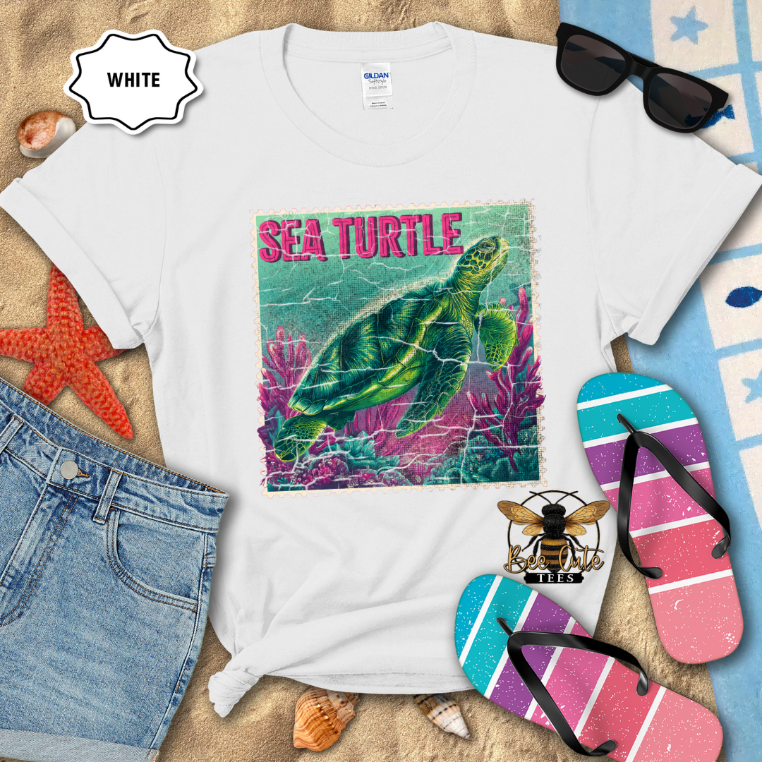 White t-shirt with sea turtle graphic on a sandy surface with beach accessories.