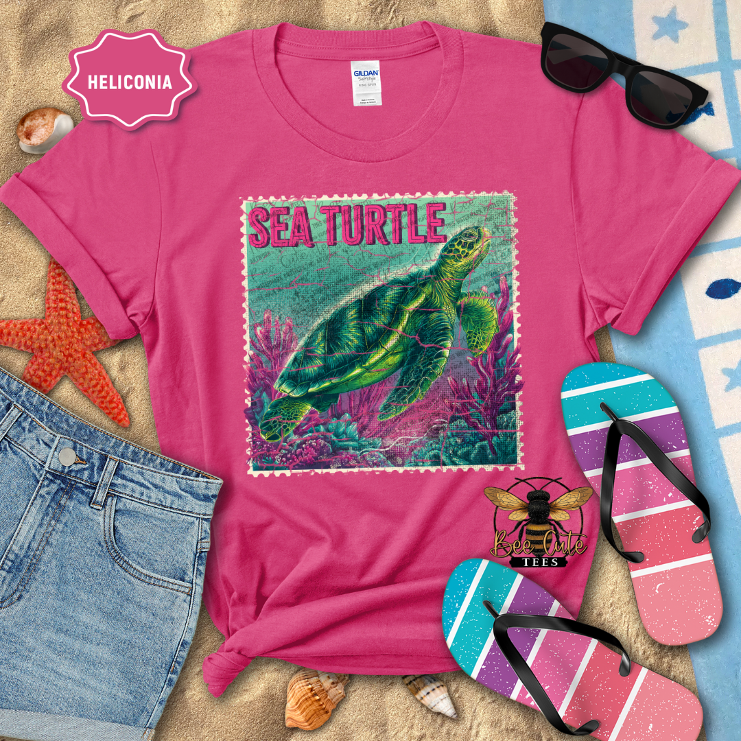 Pink t-shirt with sea turtle design on a beach setting with sunglasses and flip-flops.