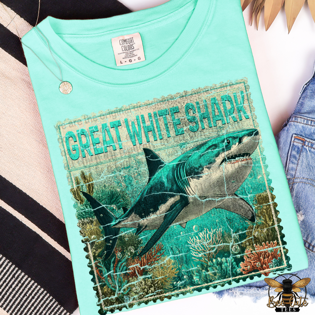 Light blue t-shirt with a graphic of a great white shark and text on a patterned surface.