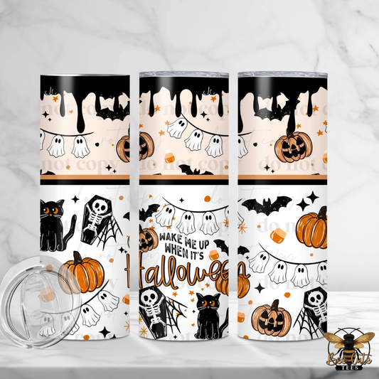 Three Halloween-themed stainless steel tumblers with a clear lid, displayed on a white marble surface. The tumblers feature a repeating pattern of orange pumpkins, black bats, white ghosts, black cats, and skeletons in orange and black.