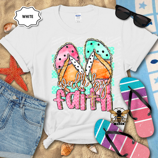 White t-shirt with 'walk by faith' design, sunglasses, denim shorts, and flip-flops on a textured surface.