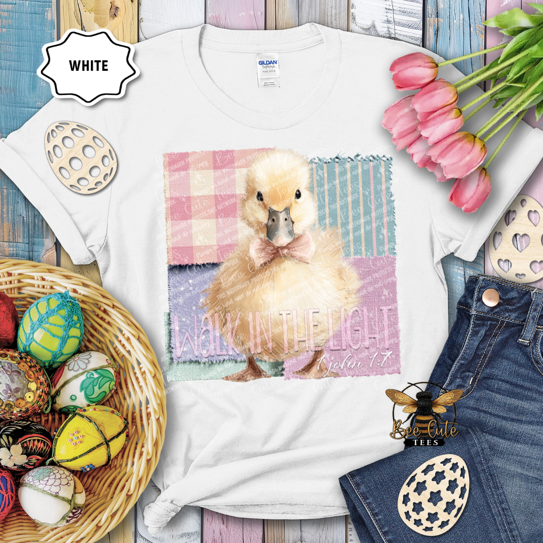 White t-shirt with a duck graphic and Easter decorations on a wooden surface.