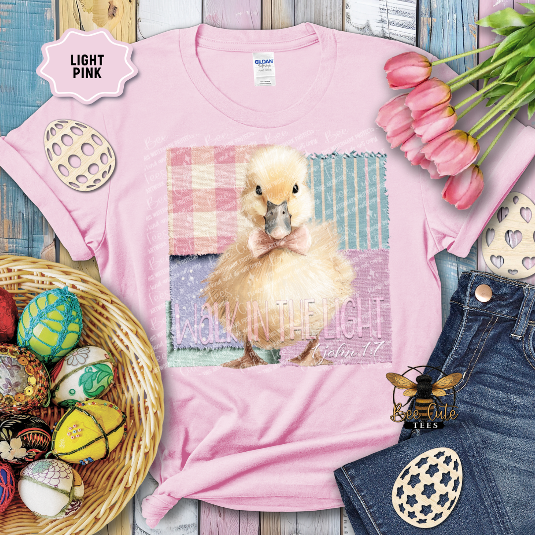 Pink t-shirt with a duck graphic and text, surrounded by Easter decorations on a wooden surface.