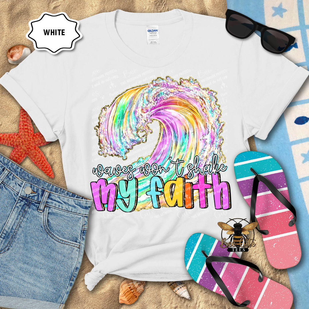 White t-shirt with colorful design and text 'waves won't shake my faith' on a beach-themed background.