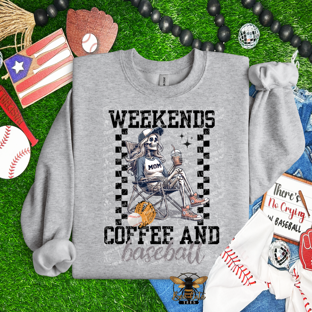 Gray sweatshirt with skeleton design and text 'Weekends Coffee and Baseball' on a grass background with sports-themed items.