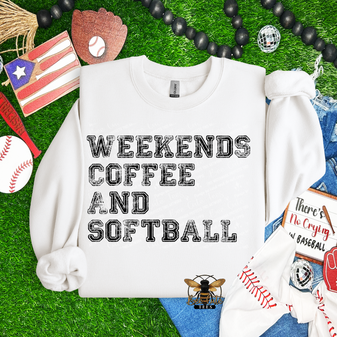 White sweatshirt with 'Weekends Coffee and Softball' text on a grass background with sports-themed accessories.