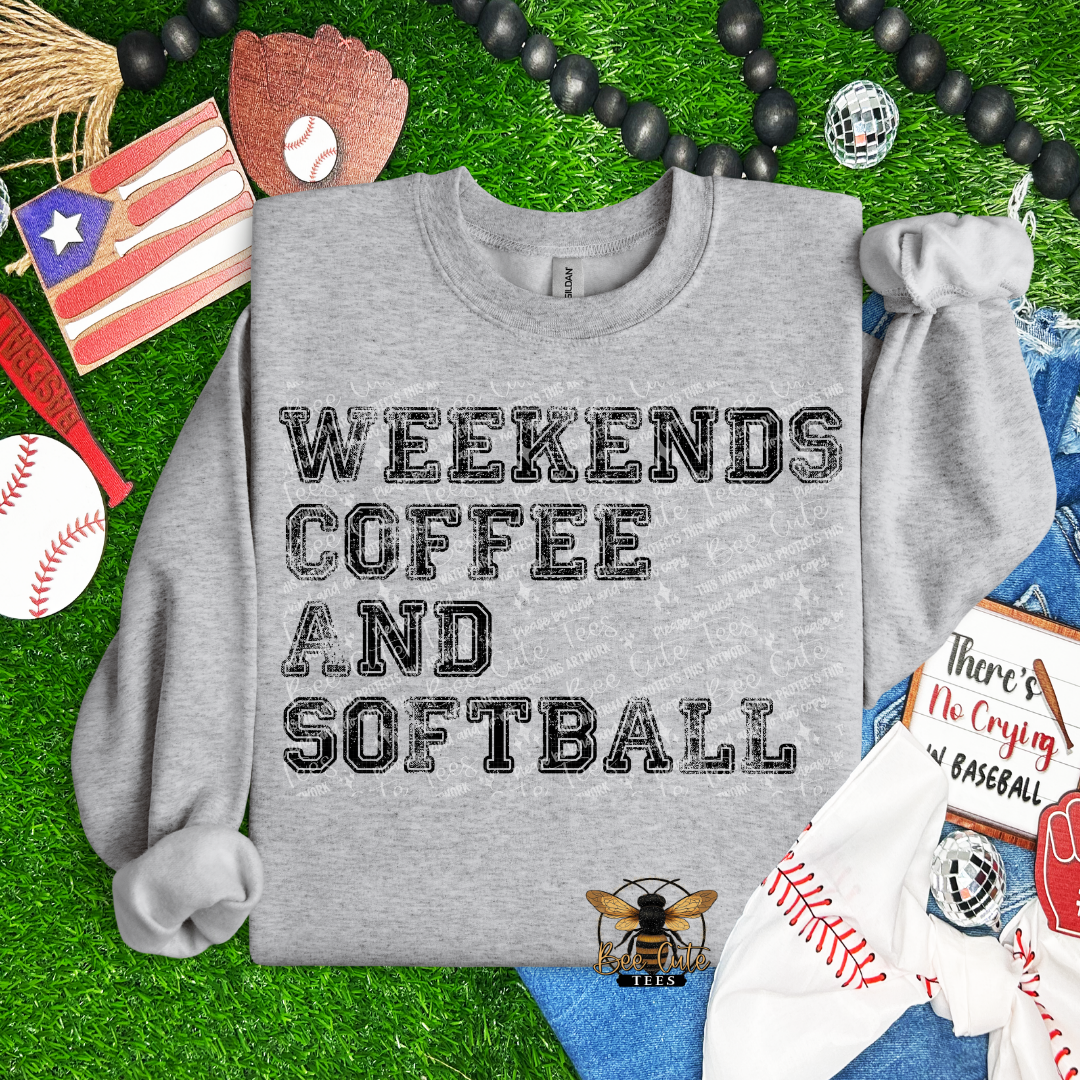 Gray sweatshirt with 'Weekends Coffee and Softball' text on a grass background with sports-themed items.