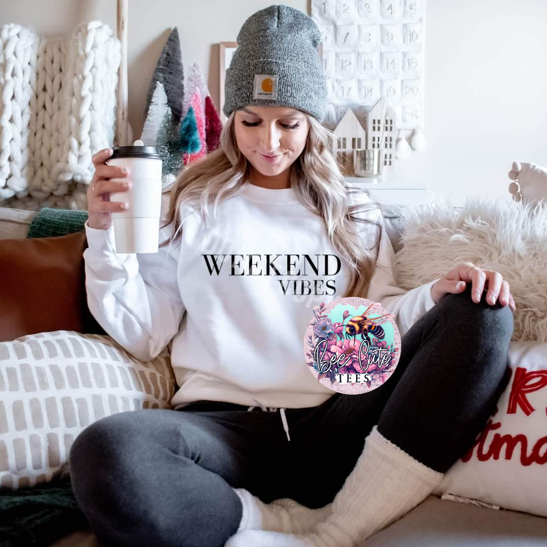 Person wearing a 'Weekend Vibes' sweatshirt, holding a coffee cup, and sitting on a couch.
