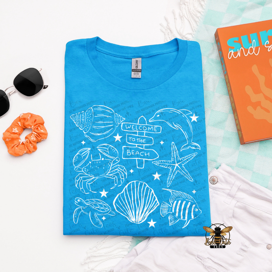 Blue t-shirt with beach-themed design on a white surface with accessories.
