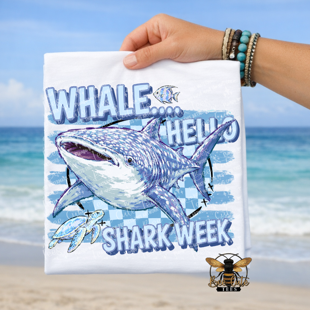A hand holds a white graphic T-shirt featuring a large shark illustration and the text 'WHALE.