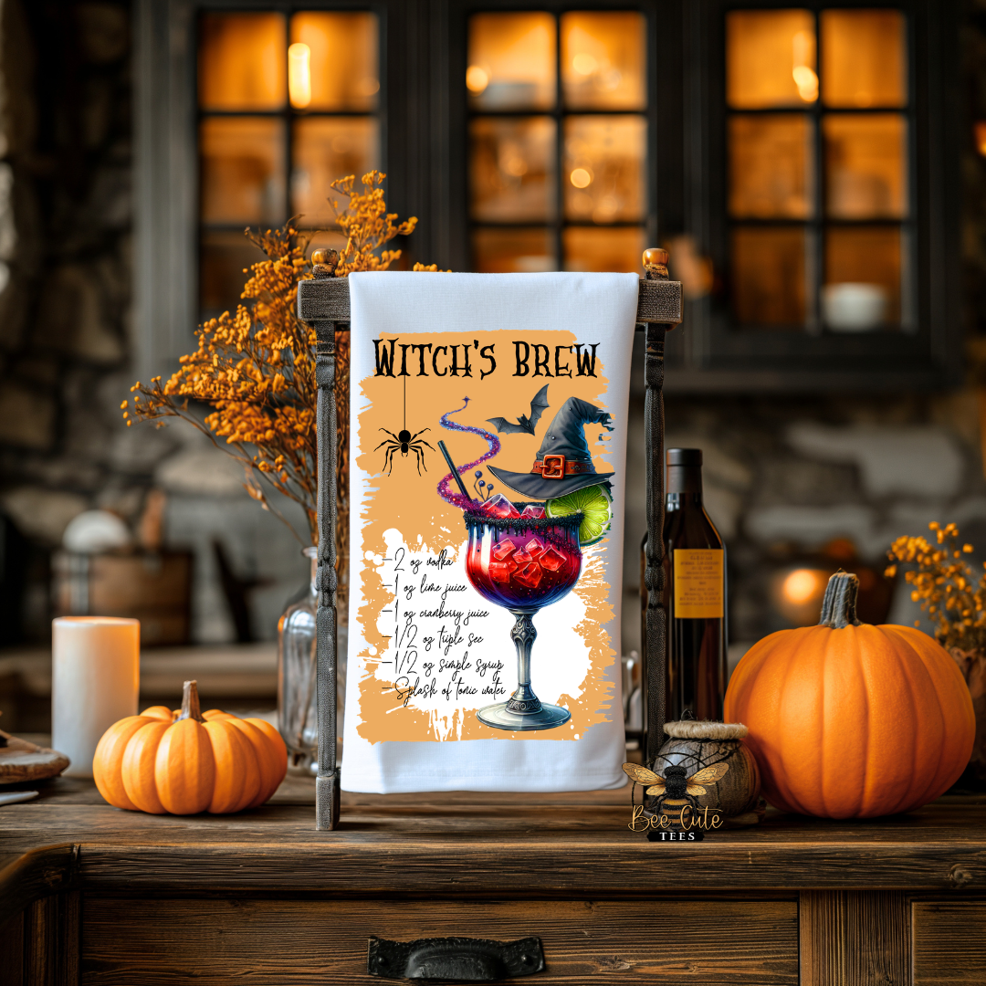 A Halloween-themed kitchen towel displayed on a wooden stand on a rustic wooden table. The towel features a colorful graphic of a witch's potion in a goblet, a black witch hat, a spider, and the text 'WITCH'S BREW' along with a poem.