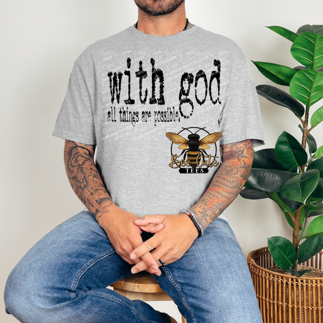 Person wearing a gray t-shirt with a bee logo and text, sitting next to a plant.